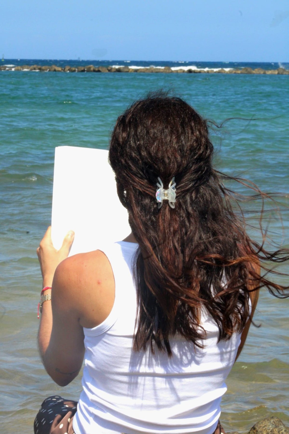 Vanesa Peña de espaldas, leyendo frente al mar